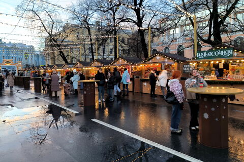 Люди за столиками с едой напротив торговых палаток